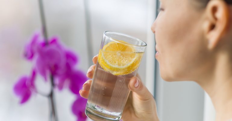 Woman drinking summer refreshing fruit flavored infused water with fresh organic lemon.
