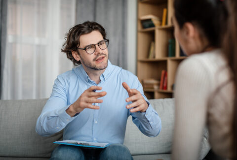 Emotional young european guy doctor speaks and gesticulates with woman patient in office clinic interior