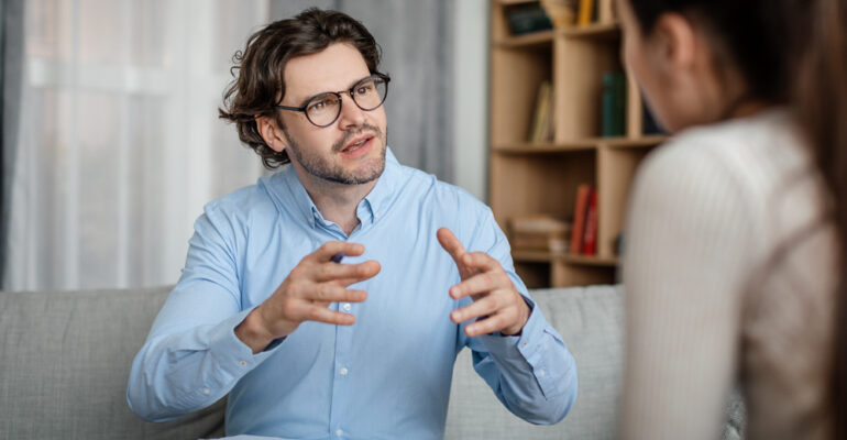 Emotional young european guy doctor speaks and gesticulates with woman patient in office clinic interior