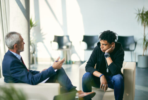 Black teenage boy communicating with mature psychotherapist during session at counselling center.