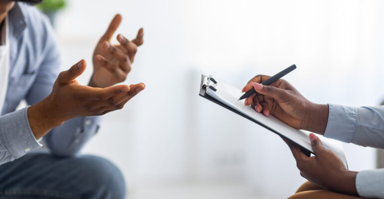 Professional psychological help concept. Unrecognizable black man talking to psychotherapist at office, closeup view