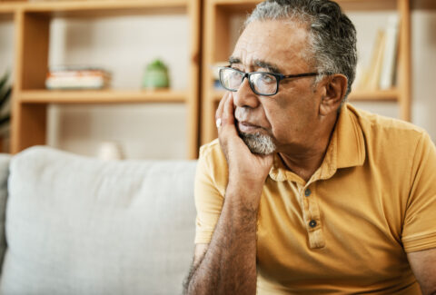 Face, depression and thinking with a sad old man on a sofa in the living room of his retirement home. Mental health, alzheimer or dementia and a senior person looking lonely with memory nostalgia