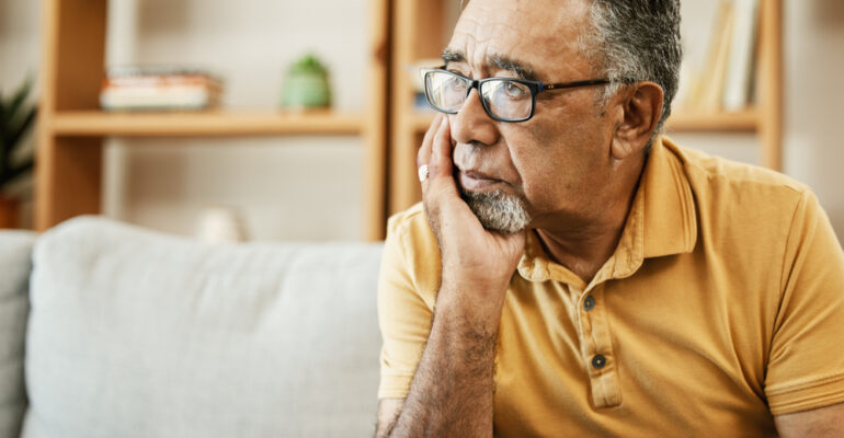 Face, depression and thinking with a sad old man on a sofa in the living room of his retirement home. Mental health, alzheimer or dementia and a senior person looking lonely with memory nostalgia