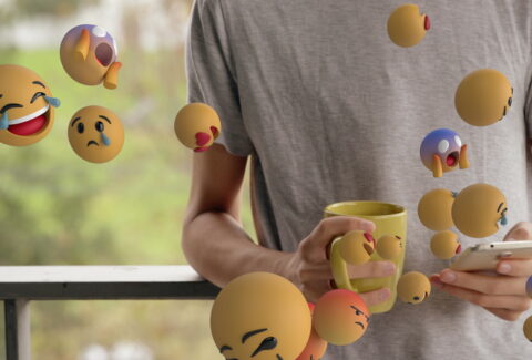 Holding smartphone and mug, person surrounded by floating emojis, engaging online. Social media, technology, communication, digital, networking, connectivity