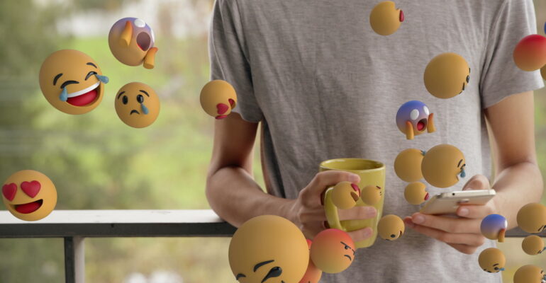 Holding smartphone and mug, person surrounded by floating emojis, engaging online. Social media, technology, communication, digital, networking, connectivity